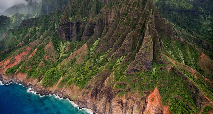 De dramatische smaragdgroene bergkammen van de Nā Pali Coast die hoog boven de kolkende blauwe Stille Oceaan uitsteken.