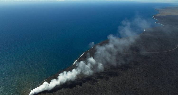Luchtfoto van vulkanische stoomwolken die de Stille Oceaan ontmoeten aan de rand van een lavavlakte.