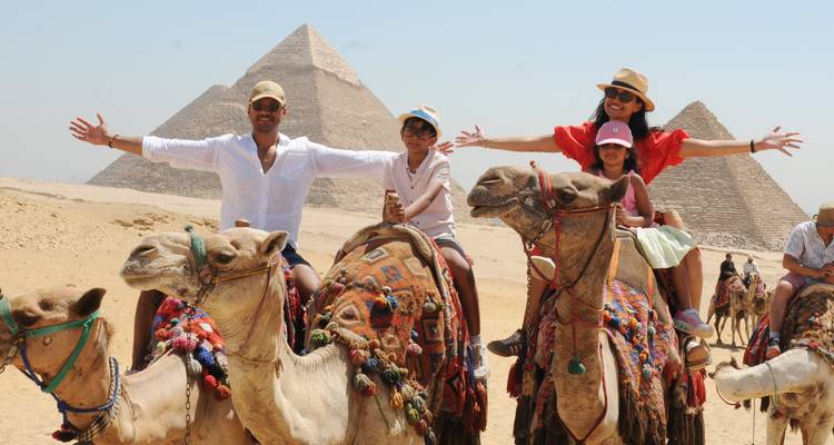 Une famille étend les bras tandis qu'elle fait du chameau devant les pyramides.