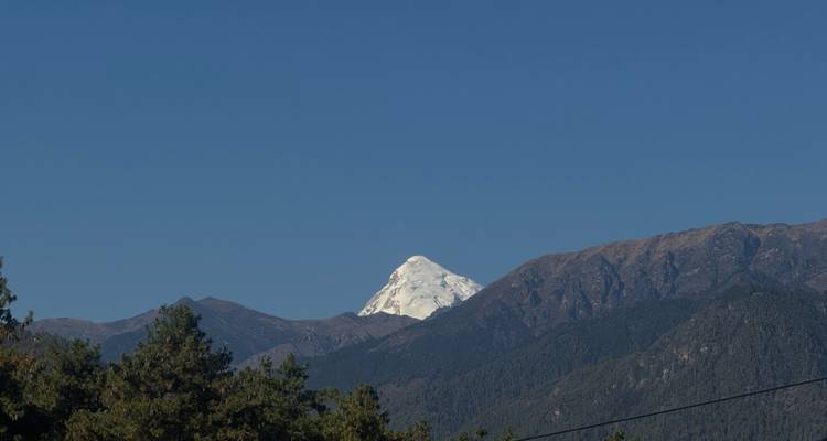 Le pic enneigé s'élève au-dessus des contreforts boisés du Bhoutan sous un ciel bleu dégagé.