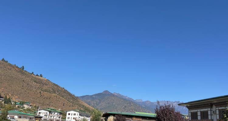 Vaste ciel bleu au-dessus d'une petite ville de vallée bhoutanaise nichée entre des collines arides et des pics verdoyants.