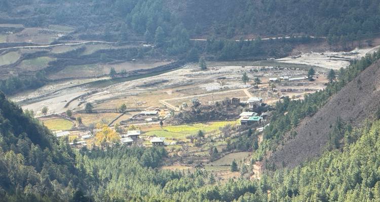 Vue aérienne d'une vallée rurale au Bhoutan montrant des terres agricoles, des maisons dispersées et une rivière sinueuse.