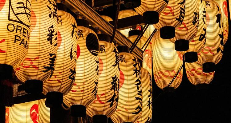 Gros plan de lanternes en papier japonais illuminées avec calligraphie, suspendues en rangées la nuit.
