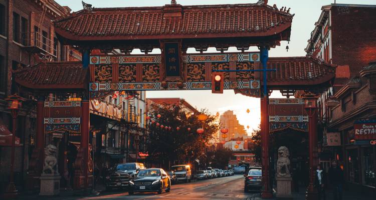 Portail ornementé rouge de Chinatown surplombant une rue du centre-ville illuminée par la lumière chaude du coucher de soleil avec des voitures et des lanternes.