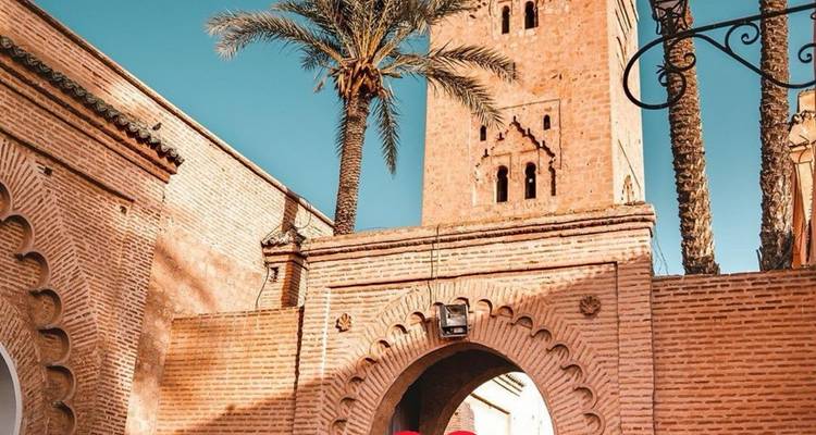 Minaret historique et arcade encadrés par des palmiers sous un ciel bleu dégagé avec un cœur en superposition en bas.