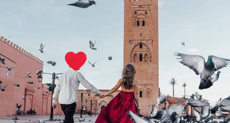 Couple dans une place remplie de pigeons se dirigeant vers une tour historique, les visages cachés par un graphique en forme de cœur.