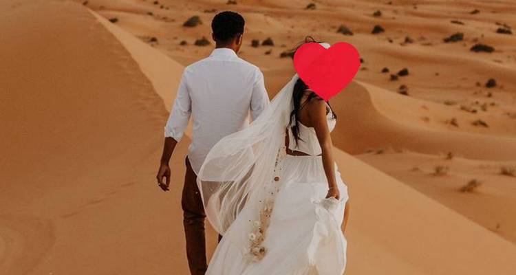 La mariée et le marié marchant sur des dunes de sable orange avec un graphique en forme de cœur sur le visage de la mariée.