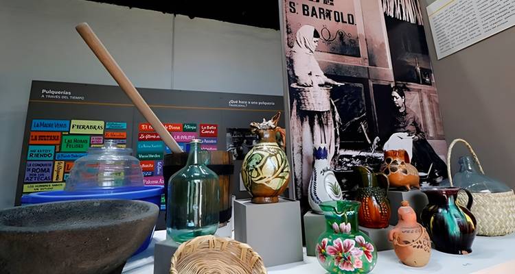 Museumsausstellung mit farbenfroher mexikanischer Keramik und Glaswaren, die auf Sockeln angeordnet sind, mit Informationstafeln im Hintergrund.