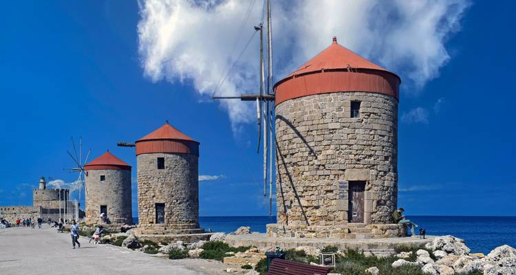 Drei historische Steinwindmühlen in einer Reihe an der Rhodos-Wasserkante unter einem leuchtend blauen Himmel