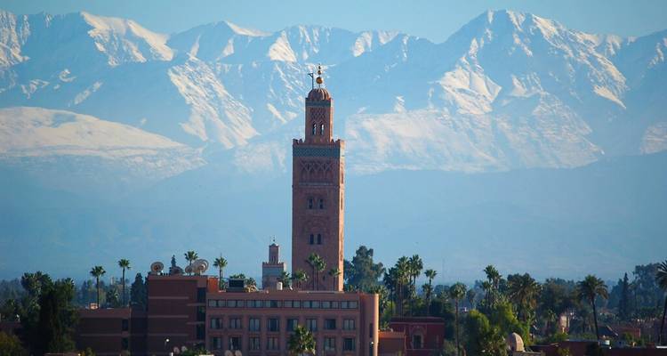 La tour de la Mosquée Koutoubia s'élevant au-dessus de l'horizon de Marrakech avec les montagnes de l'Atlas enneigées en arrière-plan.