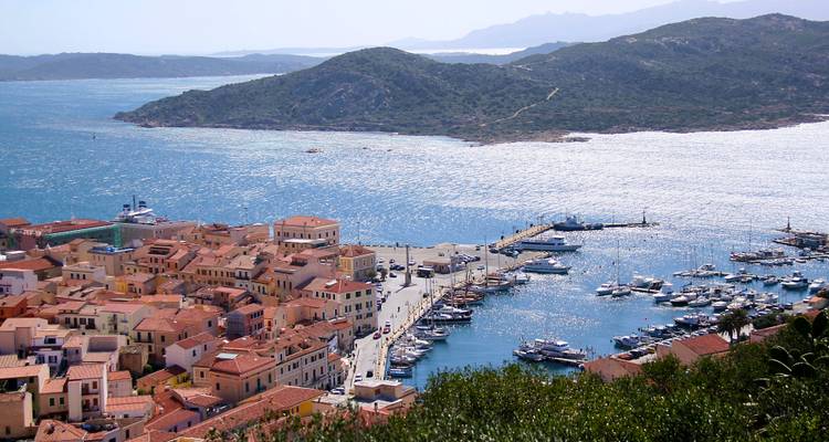 Panoramablick auf einen mediterranen Hafen mit Terrakotta-Dächern, Marina voller Yachten und bergigen Inseln in der Ferne.
