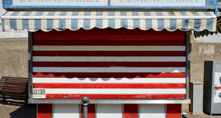 Geschlossener rot-weiss gestreifter Strandkiosk mit einem Vintage-Vordach vor einer Betonwand.