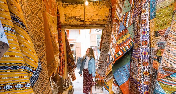 Mujer admirando coloridas alfombras tejidas colgadas en un estrecho pasaje del zoco