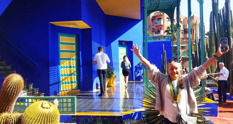 Visitante lleno de energía levantando los brazos en el vibrante patio azul del Jardín Majorelle en Marrakech