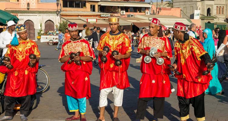 Músicos con ropa tradicional roja tocando castañuelas metálicas en la plaza de Marrakech