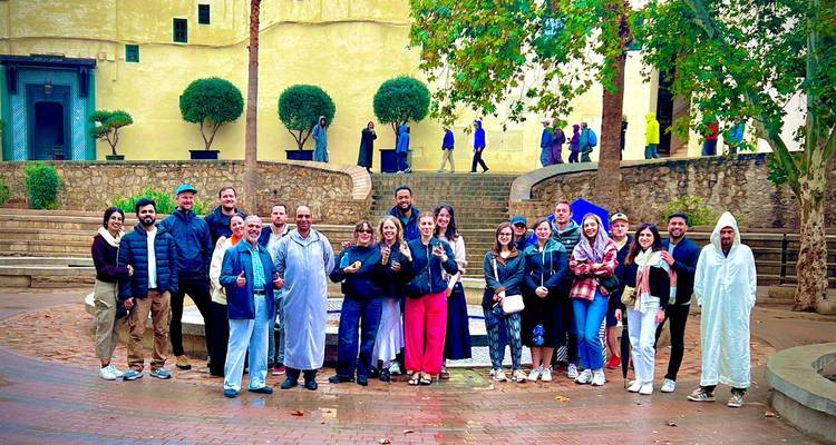 Un grupo grande de turismo posando juntos en un patio con árboles podados y escaleras de piedra detrás de ellos