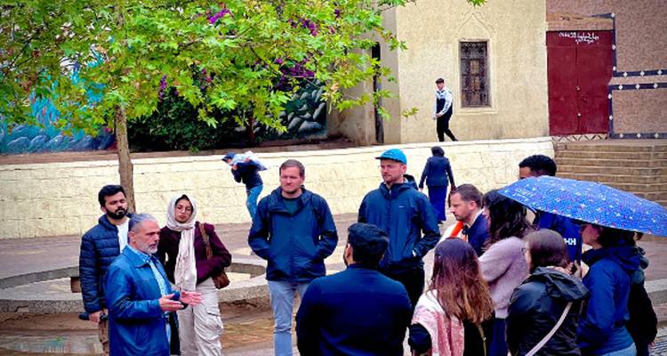 Guía hablándole a un pequeño grupo de viajeros en una calle mojada cerca de murallas históricas y árboles
