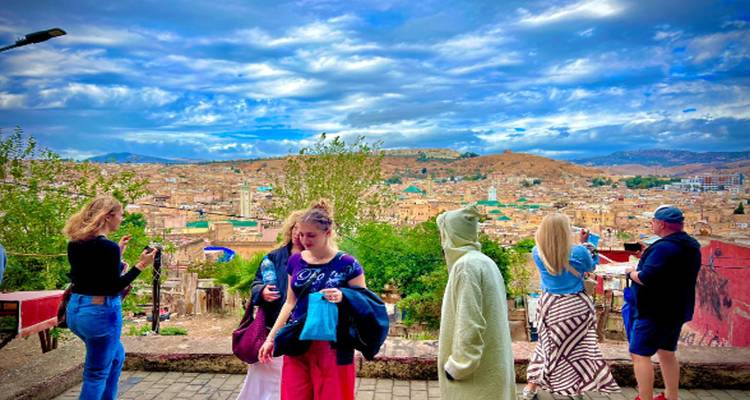 Viajeros tomando fotos en un mirador con vista a una ciudad extendida en las laderas bajo nubes dramáticas