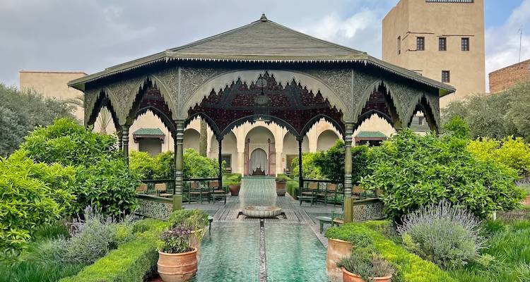 Pabellón elegante con arcos ornamentados, una fuente central y un exuberante jardín verde rodeando una piscina reflectante