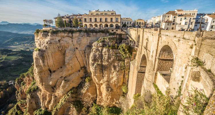 Die dramatische Klifftownstadt Ronda mit ihrer Steinbrücke, die sich über eine tiefe Schlucht unter blauem Himmel erstreckt.