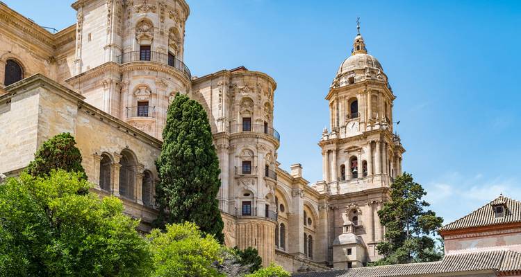 Elegante Kalksteinfassade und Glockenturm der Kathedrale von Málaga vor einem klaren blauen Himmel.