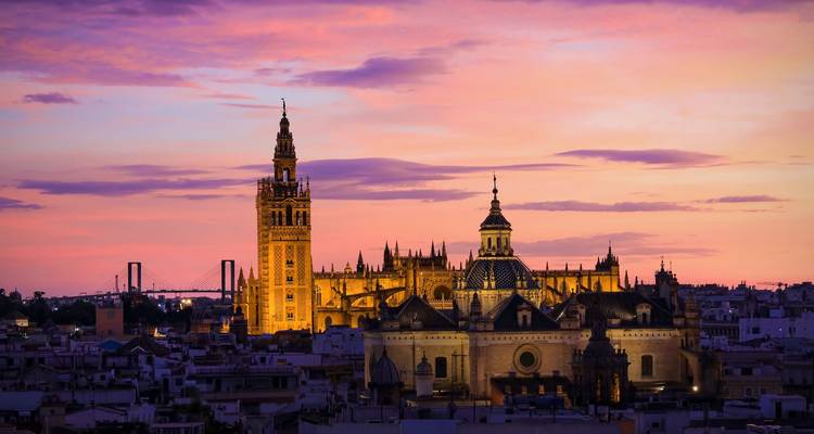 Der Sevilla-Dom und der Glockenturm Giralda leuchten bei Sonnenuntergang gegen einen leuchtend purpur-orangen Himmel.