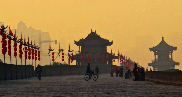 Fietsers en voetgangers op de oude stadsmuur van Xi'an, afgetekend tegen het mistige gouden avondlicht, met rode lantaarns langs de wallen