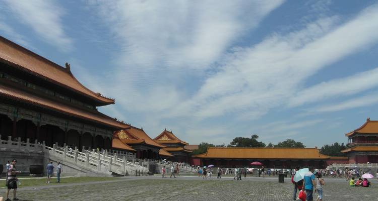 Uitgestrekt binnenplein van Peking's Verboden Stad met versierde rode daken en zalen onder een gestreepte blauwe lucht