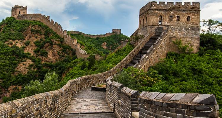 Iconische Chinese Muur die zich slingerend uitstrekt over weelderige groene heuvels onder een dramatische lucht