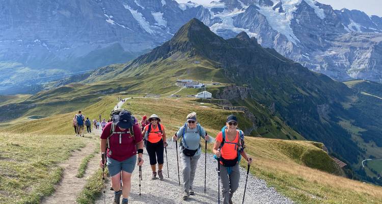 Groupe de randonneurs utilisant des bâtons montant un sentier alpin avec des pics emblématiques en arrière-plan.