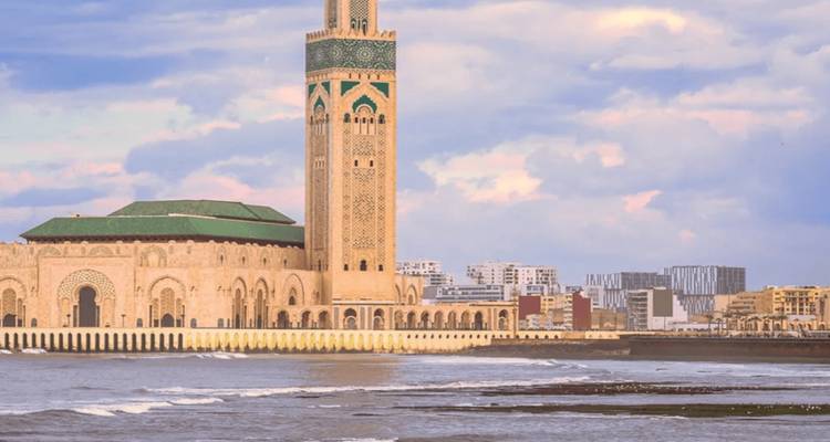 Hassan II Mosque rising above the Atlantic waves with city skyline in the background.