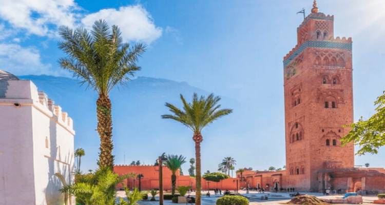Koutoubia Mosque towering over Marrakech’s square framed by palm trees and blue sky.