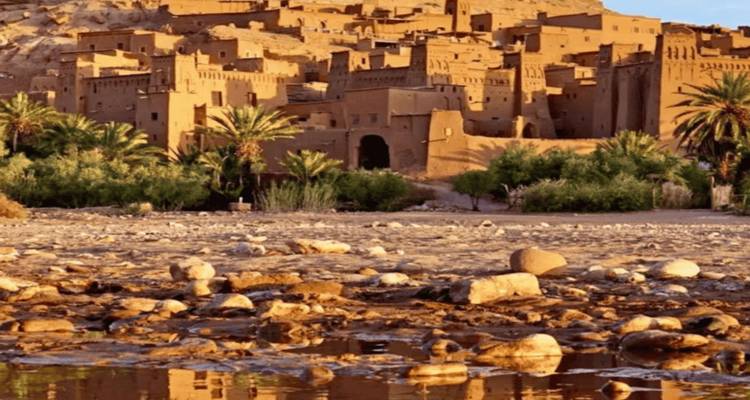 View of the earthen ksar of Aït Benhaddou across a rocky riverbed.