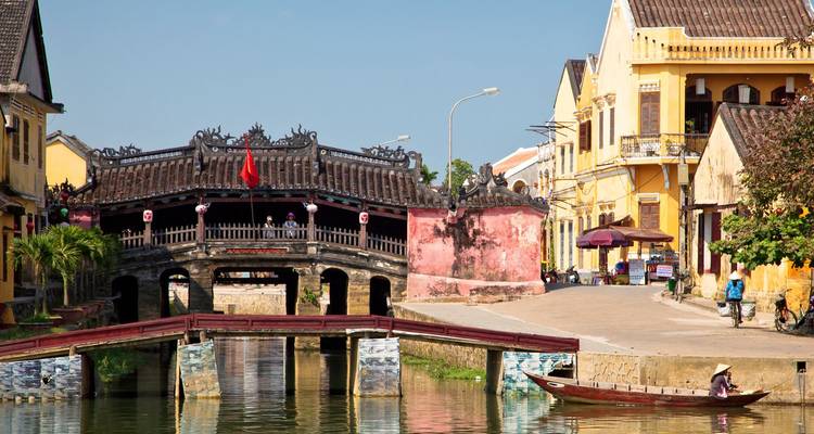 Japanse dekte brug die een kalme kanaal overspant tussen historische gele gebouwen in Hoi An