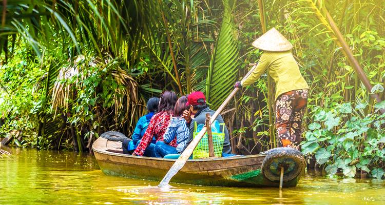 Wooden sampan navigates lush canals of the Mekong Delta steered by conical-hat local