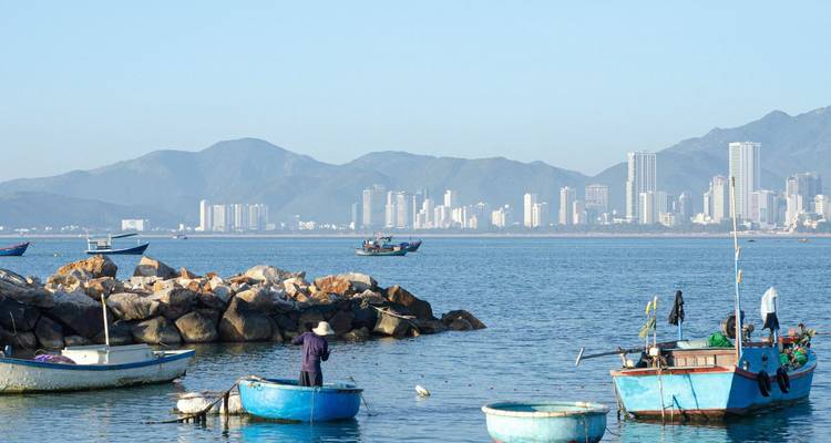 Local fisherman works from blue coracle boats off the Nha Trang coast with city skyline behind
