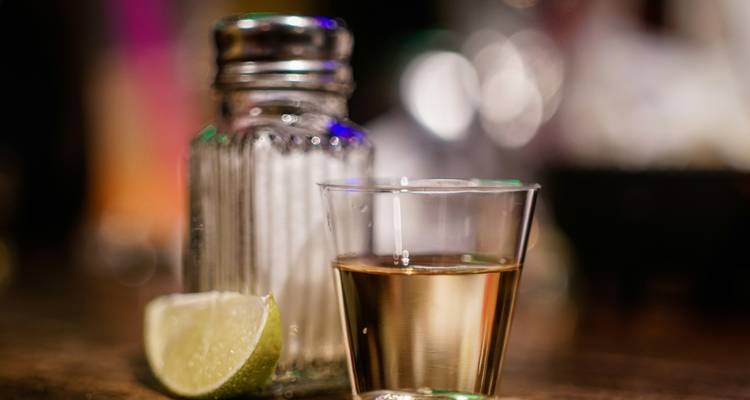 Ein einzelner Tequila-Shot mit Limettenkeil und Salzstreuer auf einer Holztheke an der Bar