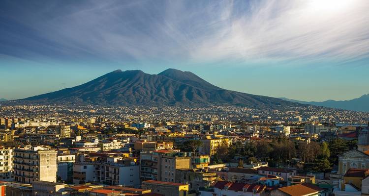 Vue panoramique sur la ville de Naples avec l'imposant mont Vésuve dominant l'horizon sous des nuages striés.