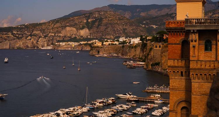 Marina bordée de yachts le long de la ville côtière de Sorrento au coucher du soleil avec des montagnes escarpées en arrière-plan.