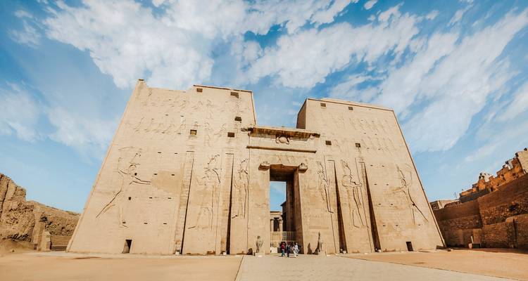 Façade massive en grès et pylônes d'un temple égyptien antique sous un ciel bleu dramatique.