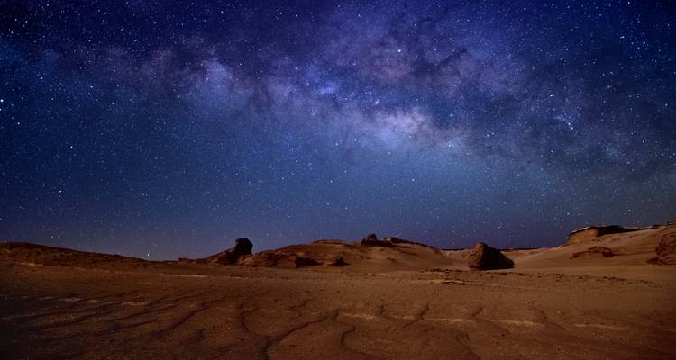 La Voie lactée parsemée d'étoiles s'étendant au-dessus d'un paysage désertique aride la nuit.