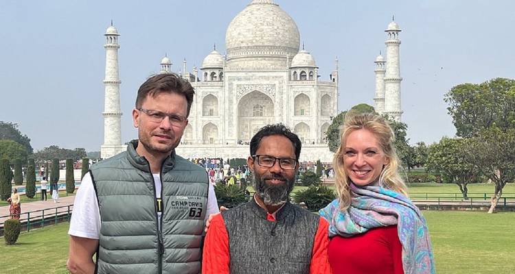 Two travellers and their guide smile for a photo with the Taj Mahal majestically framed behind them.