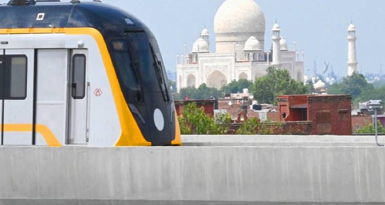 A modern metro train passes in the foreground while the iconic Taj Mahal rises in the distant skyline.