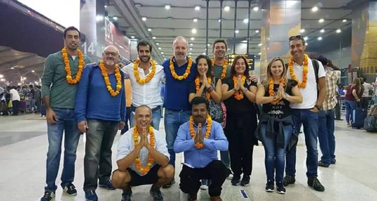 A tour group wearing marigold garlands lines up inside a brightly lit station hall for a welcome photo.