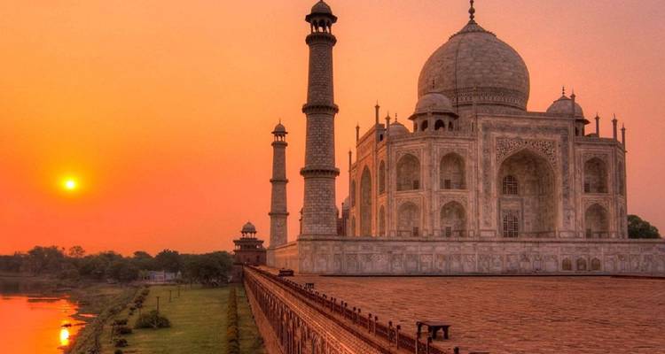 Duplicate sunset perspective of the Taj Mahal bathed in golden hues with riverbank and lawns in frame.