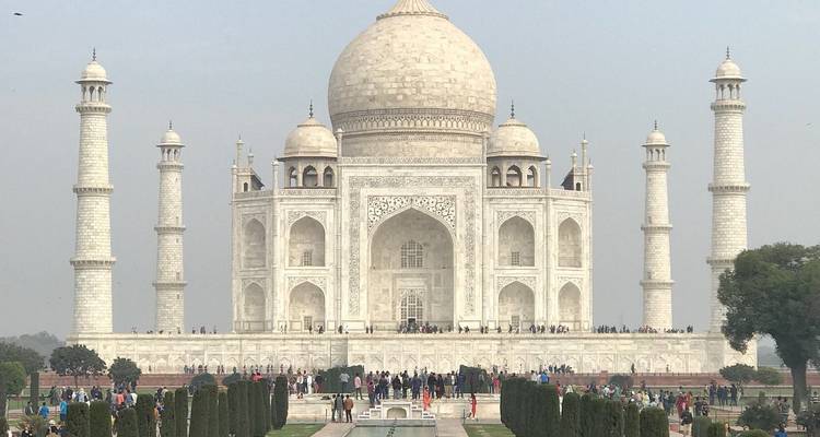 Frontal view of the Taj Mahal with its landscaped gardens and reflective pool crowded by distant visitors.