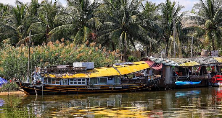 Traditionelles hölzernes Hausboot, das an einem ruhigen Backwater-Kanal mit schwankenden Kokospalmen vertäut ist.