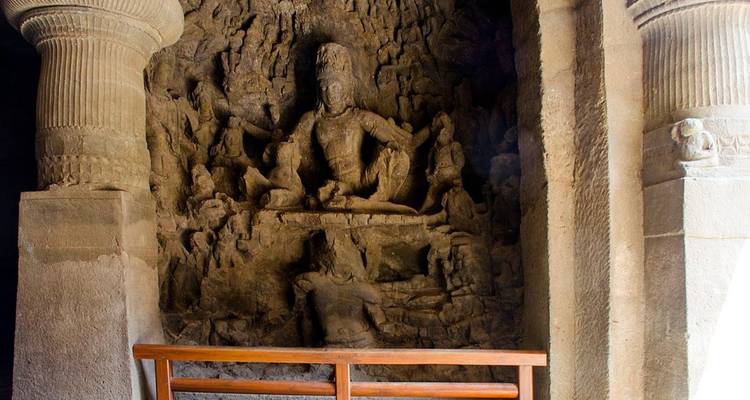 Stone sculpture of a deity inside a dimly lit rock-cut cave shrine.