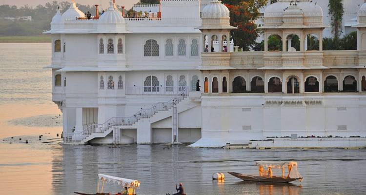 Lake Palace in Udaipur gleaming white at golden sunset as small boats glide across calm water.