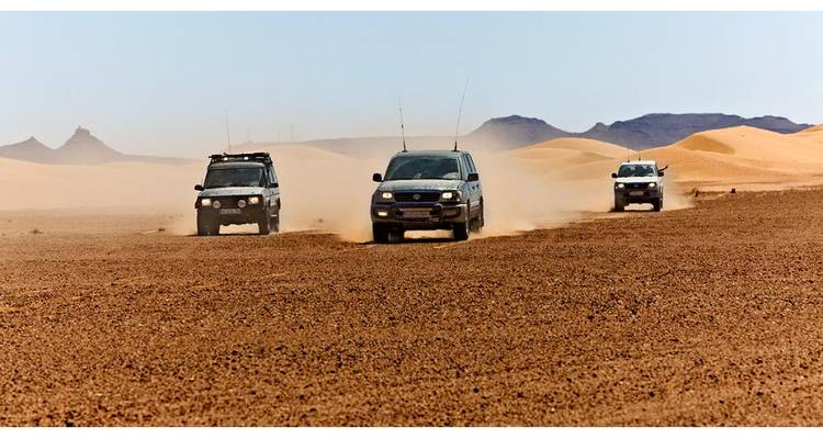 Trois véhicules tout-terrain se déplacent rapidement à travers une vaste plaine désertique marocaine en laissant des traînées de poussière